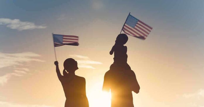 Silhouettes of a family waving American flags at sunset
