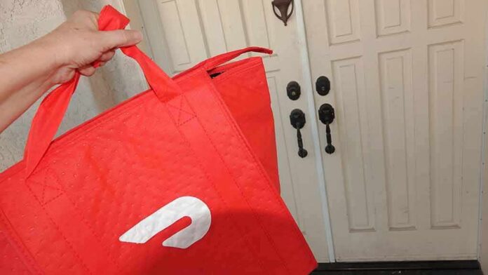 Hand holding red insulated delivery bag at a front door