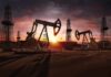 Oil pumpjacks and derricks at sunset in a desert field