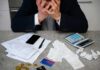 Stressed person with head in hands at a desk with bills and calculator