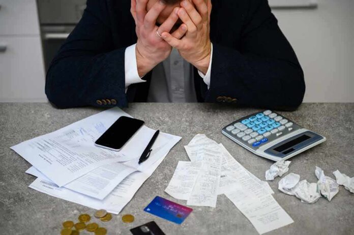 shutterstock_1730933638 Stressed person with head in hands at a desk with bills and calculator