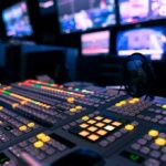 Culture-War Noise Muffles the Quid Pro Quo broadcast control room mixing console with illuminated buttons