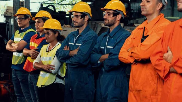 shutterstock_1905872197 Factory workers standing in a line wearing hard hats and safety gear