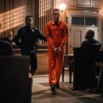 Defendant in orange jumpsuit escorted by officer in courtroom