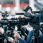 Kushner Deal Ignites 100-Day Street War Broadcast cameras on tripods at a press event