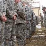 Soldiers in camouflage uniforms stand in two facing rows outdoors