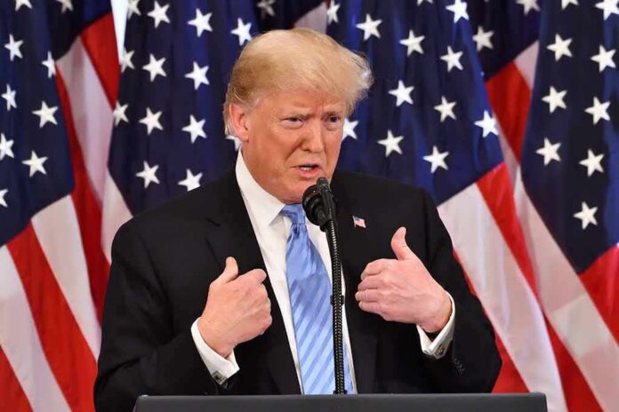 shutterstock_1200585187 Donald Trump speaking at a podium with American flags behind him