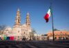 Mexican flag waving in a plaza with a historic cathedral