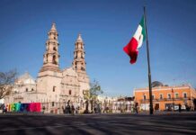 Mexican flag waving in a plaza with a historic cathedral