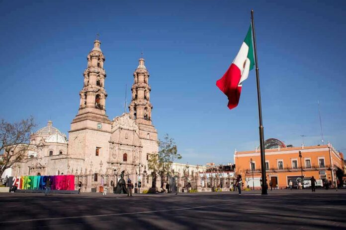 shutterstock_1317741923 Mexican flag waving in a plaza with a historic cathedral