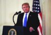 Nobel Snubs Ceasefires, Bets On Courtroom Muscle man at podium with microphone and US flag