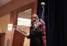 Judge-Approved Raid – Immigration Fraud Trail? Ilhan Omar speaking at a podium with a microphone