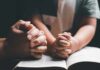 Adult and child hands clasped in prayer over an open book