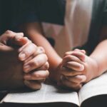 Scripture Twist? Jesus Card Sparks Texas Firestorm Adult and child hands clasped in prayer over an open book