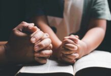 Adult and child hands clasped in prayer over an open book