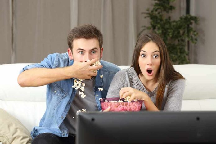 Couple watching TV with shocked expressions and popcorn bowl