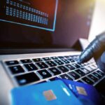 Gloved hand typing on laptop keyboard with credit cards nearby