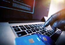 Gloved hand typing on laptop keyboard with credit cards nearby