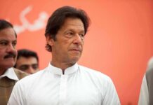 Imran Khan in a white kurta looking to the side against an orange background