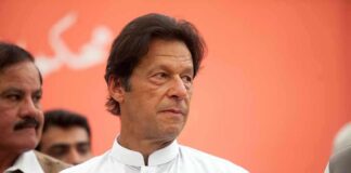 Imran Khan in a white kurta looking to the side against an orange background