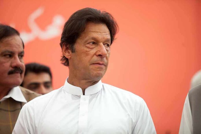 Imran Khan in a white kurta looking to the side against an orange background