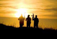 silhouettes of three armed people at sunset