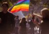 Person holding a rainbow flag at an outdoor gathering