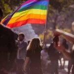 Person holding a rainbow flag at an outdoor gathering
