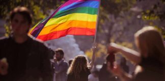 Person holding a rainbow flag at an outdoor gathering