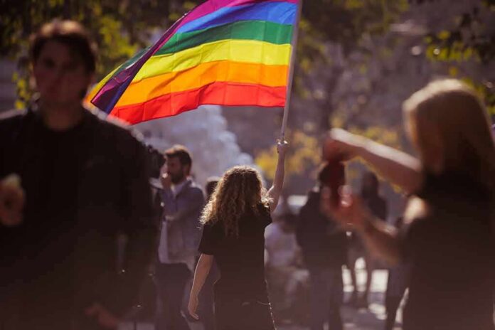 shutterstock_738837676 Person holding a rainbow flag at an outdoor gathering