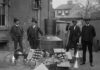 Home Distilling On The Chopping Block Four men stand around a large metal still with jars and funnels