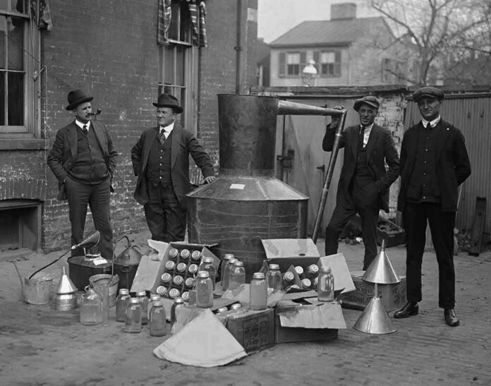 shutterstock_785840218 Four men stand around a large metal still with jars and funnels